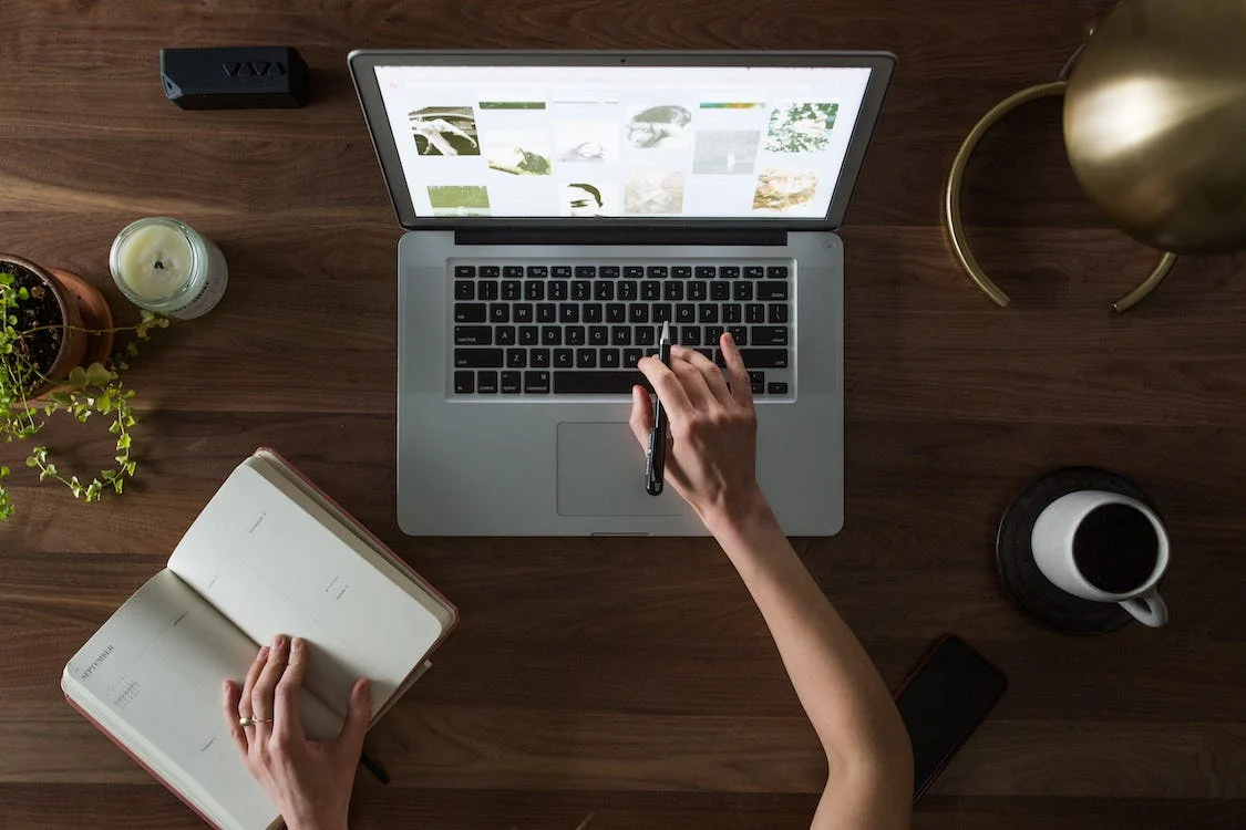 a woman working on her laptop and writing in her notebook