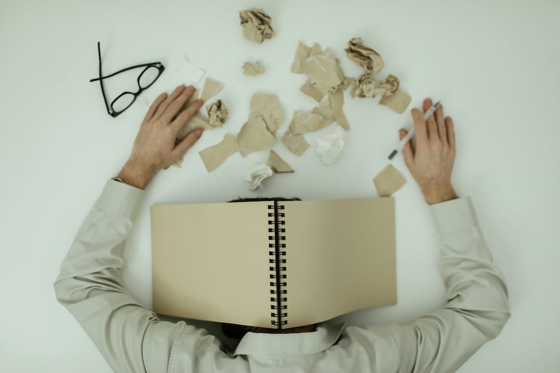 person with their head on desk and a book covering their head