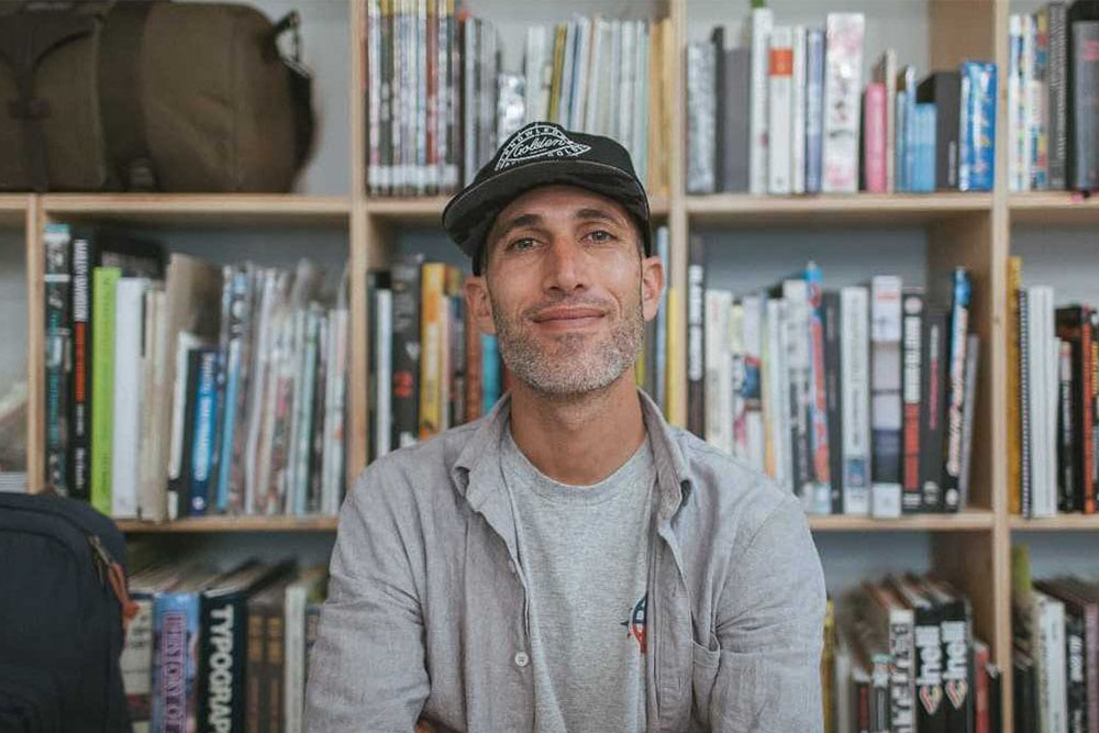 photograph of benny gold in front of bookcase wearing a hat