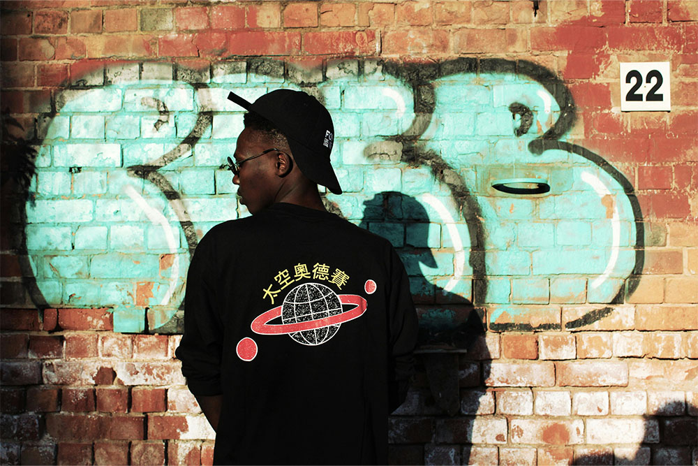 streetwear photoshoot for starting a clothing brand with black longsleeve tshirt and hat with grafiti wall in background