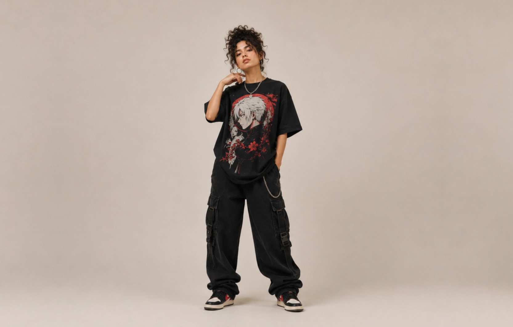 Person in an oversized black T-shirt with anime graphic, black cargo pants with a chain, posing in a studio setting.