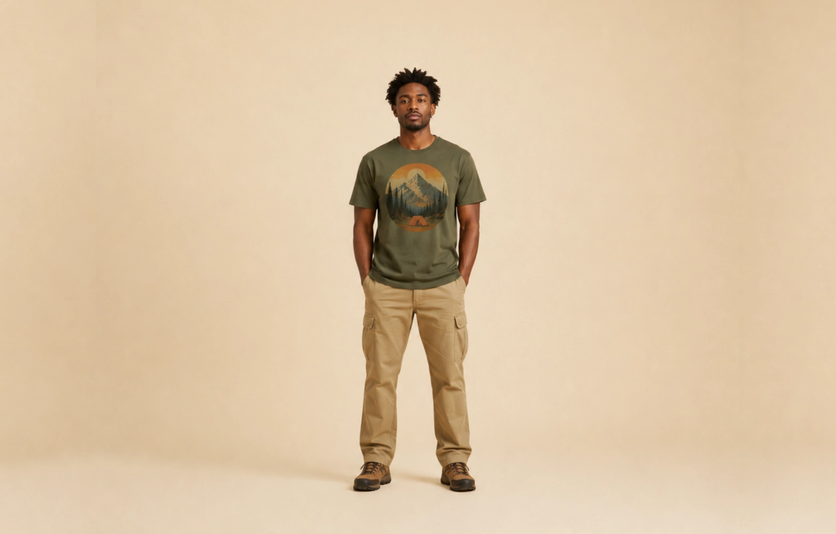 Man wearing an olive-green T-shirt with a mountain graphic and beige cargo pants, standing against a beige backdrop with hands in pockets.
