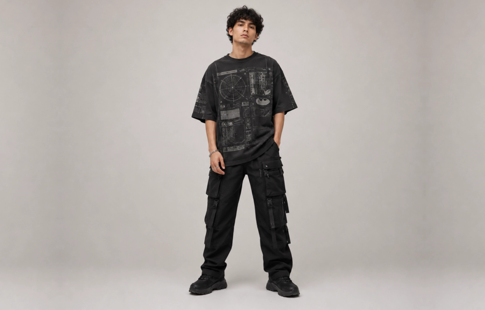 Young man wearing an oversized black graphic T-shirt and black cargo pants, standing with hands in pockets.