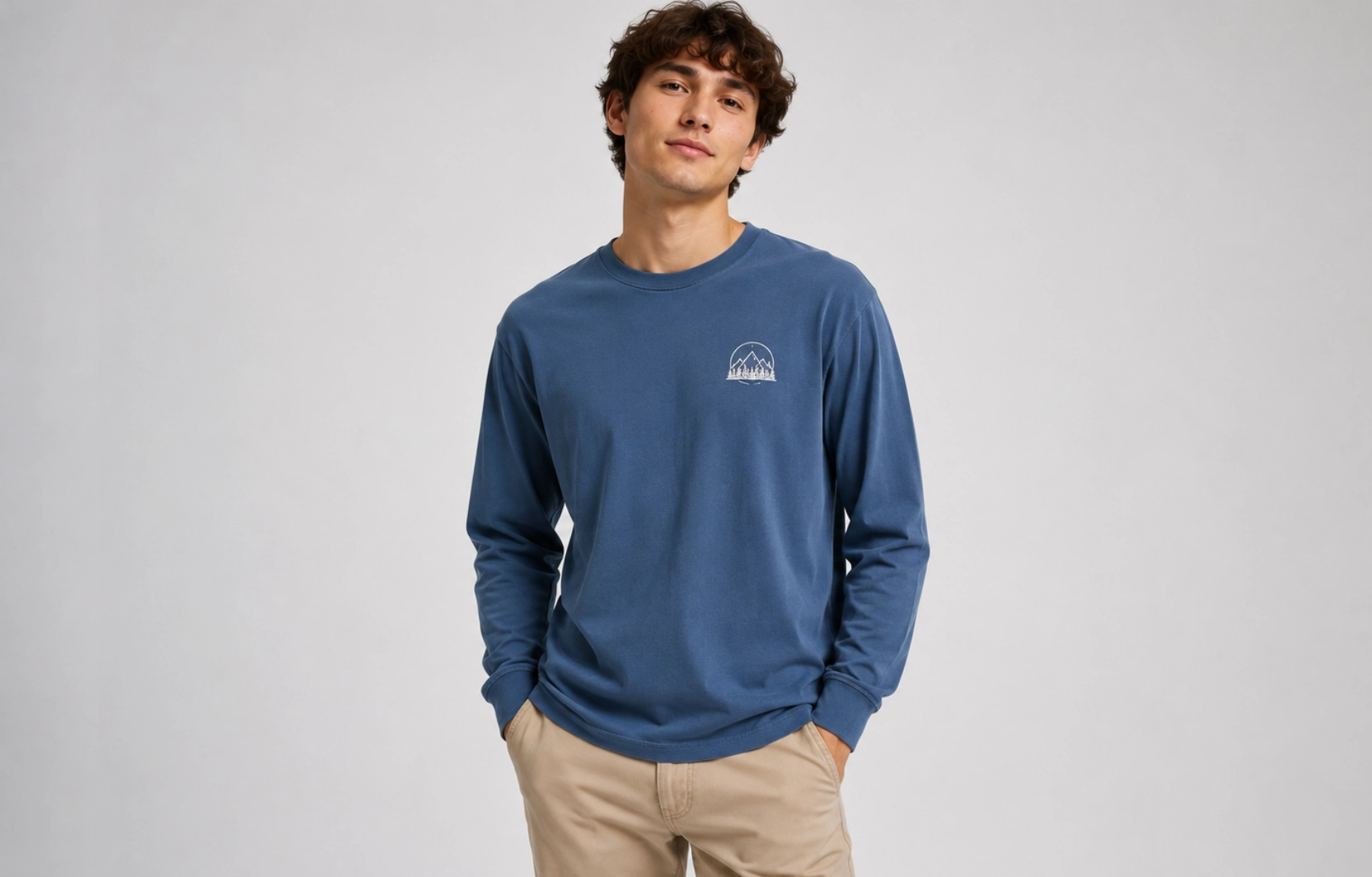 Male model wearing a blue long-sleeve shirt with a small white mountain logo on the left chest, standing against a neutral gray backdrop.