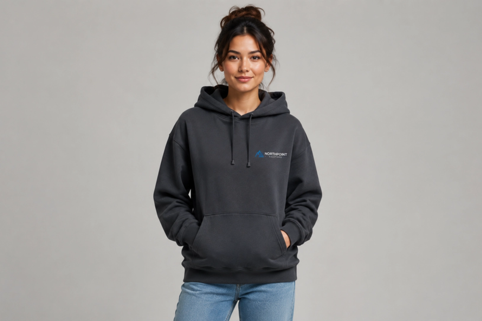 Young woman standing in front of a neutral backdrop, wearing a dark gray hoodie with a small blue Northpoint logo on the chest, hands in pockets.