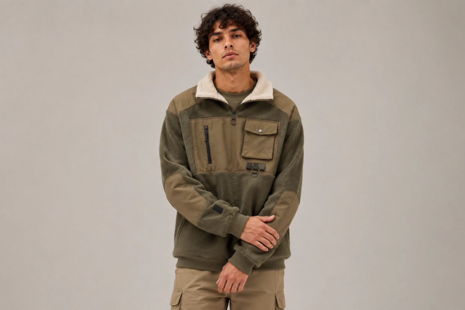Man modeling a color-block olive fleece jacket with a cream sherpa collar and multiple pockets, neutral backdrop.