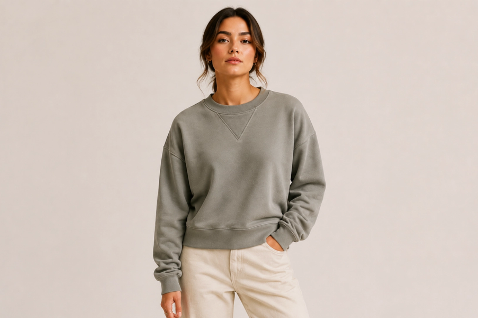 Woman wearing a gray-green sweatshirt and beige pants, standing against a neutral backdrop.