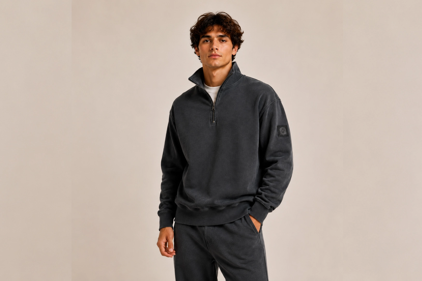 Man wearing a dark gray fleece pullover with a zip collar, standing against a beige backdrop.
