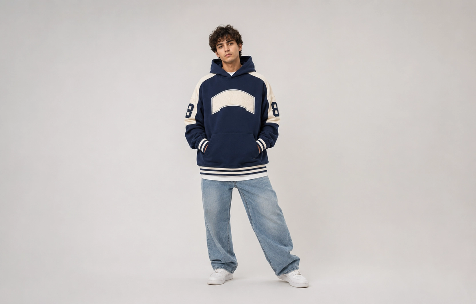 Young man in a navy hoodie with cream panels, front pocket, and striped cuffs, posing against a light gray backdrop.