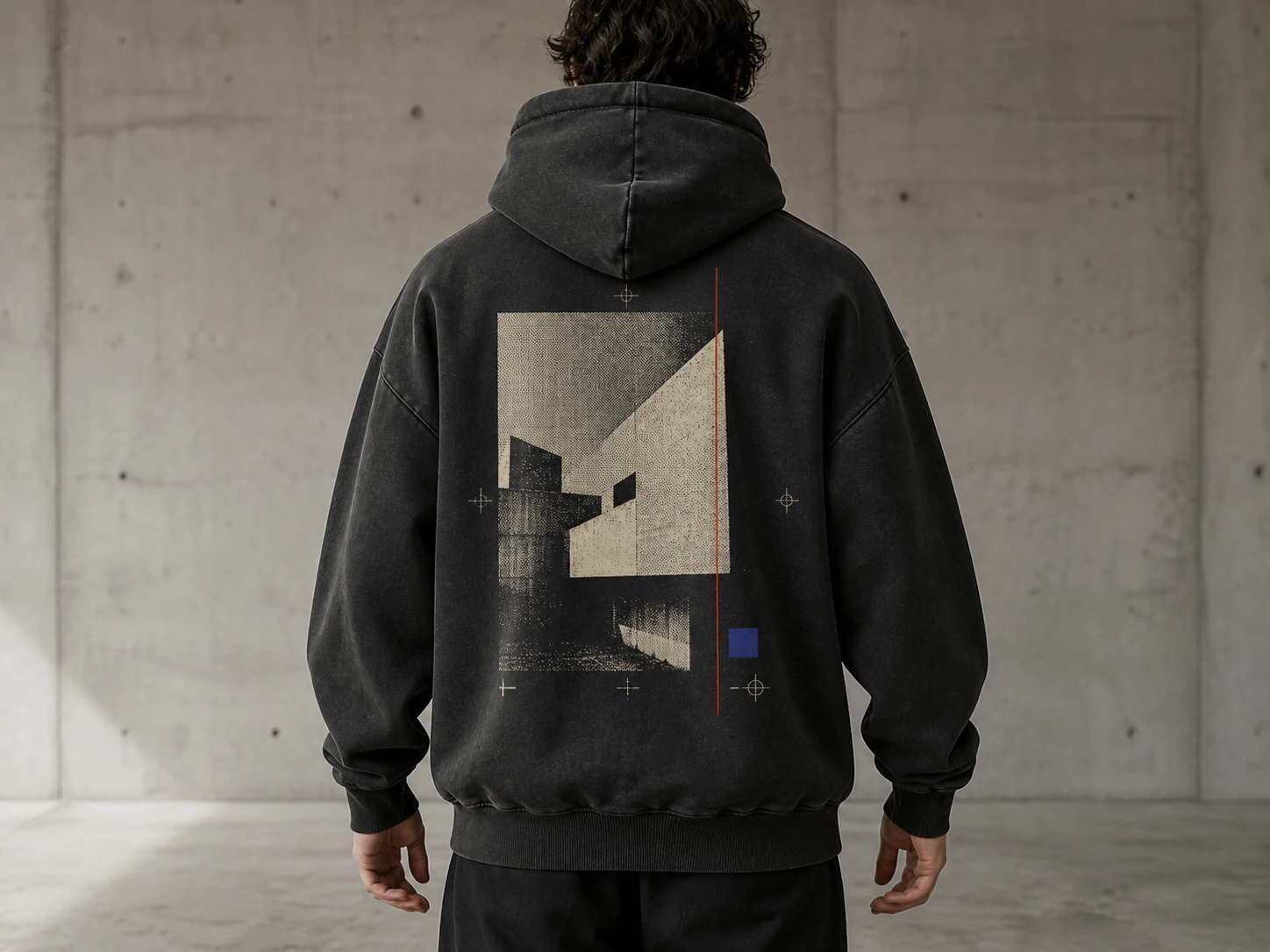 A person in a black hoodie with abstract geometric art stands in a concrete room, facing away, creating a modern, urban vibe.