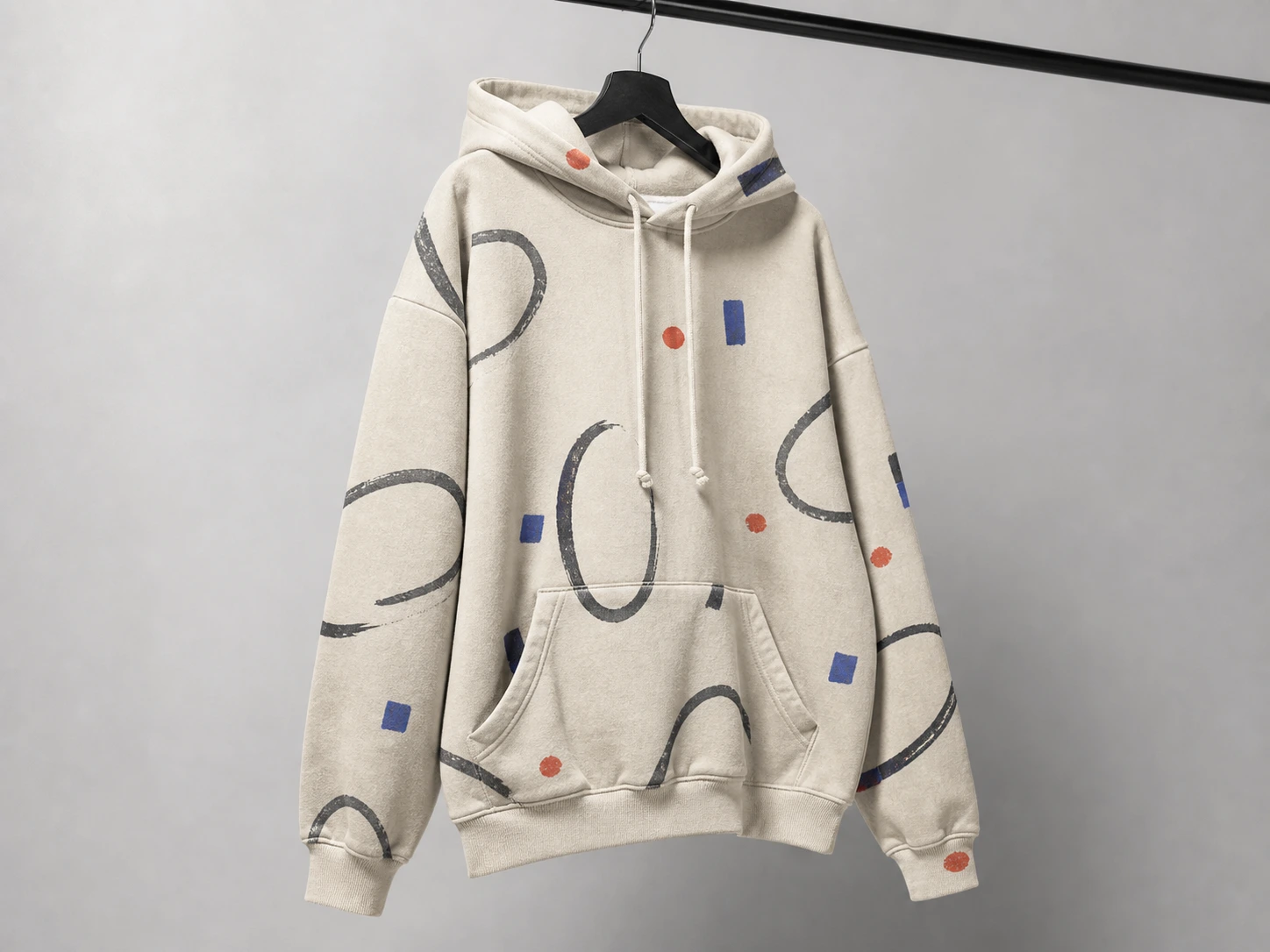 Beige hoodie with abstract black, blue, and orange shapes, hanging on a black hanger against a light gray background.