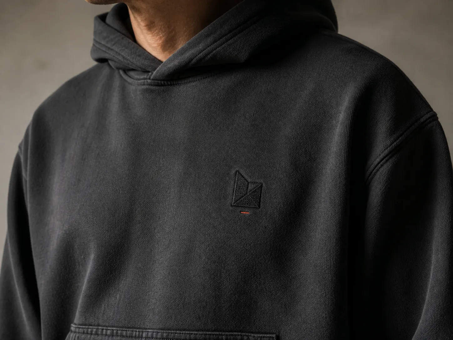 Close-up of a person wearing a black hoodie with a subtle logo on the chest, set against a neutral background.
