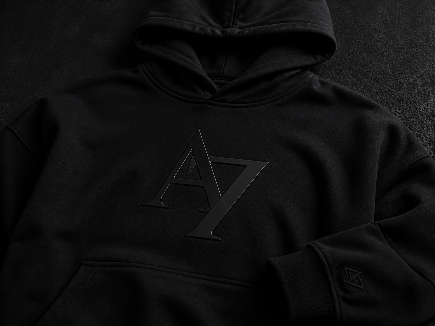 Black hoodie with embossed "A7" logo on chest and sleeve, laid on a dark surface, showcasing minimalist design and style.