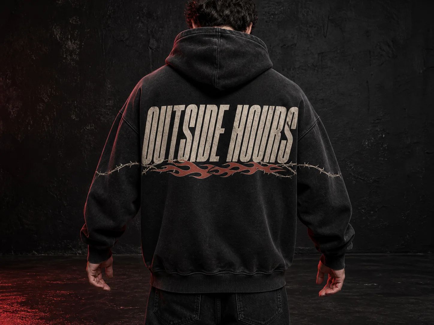 Person in black hoodie with "OUTSIDE HOURS" text and barbed wire design stands against a dark background, facing away.