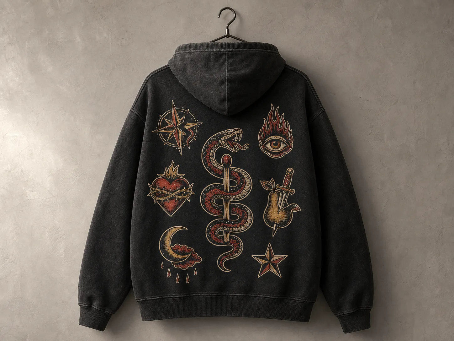 Black hoodie with vintage tattoo designs: snake, heart, eye, dagger, star, and compass. Hanging on a wall hook.