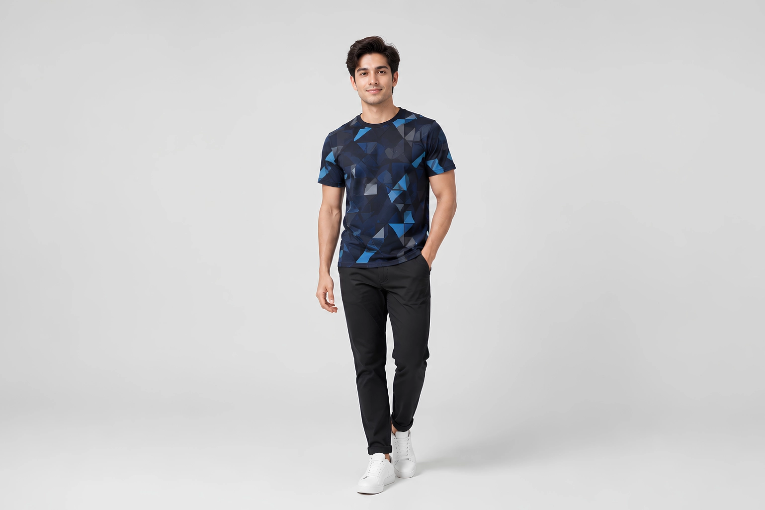 Man in geometric blue shirt, black pants, and white sneakers stands confidently against a plain gray background.