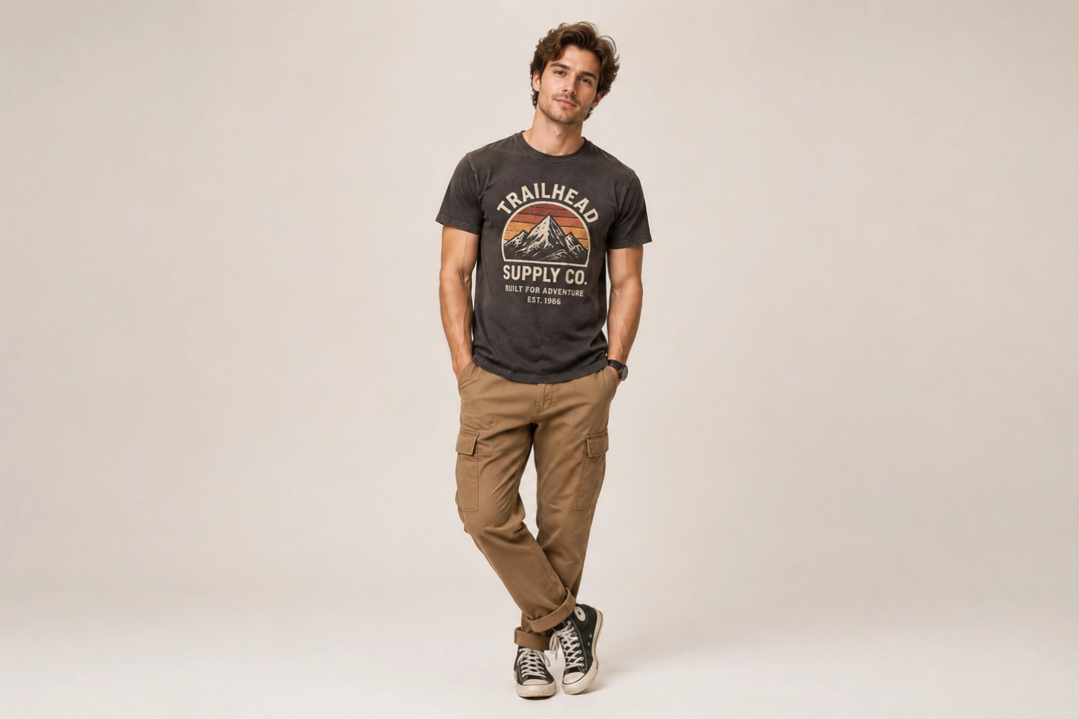 Studio portrait of a man in a black graphic T-shirt, tan cargo pants, and sneakers, standing with hands in pockets.